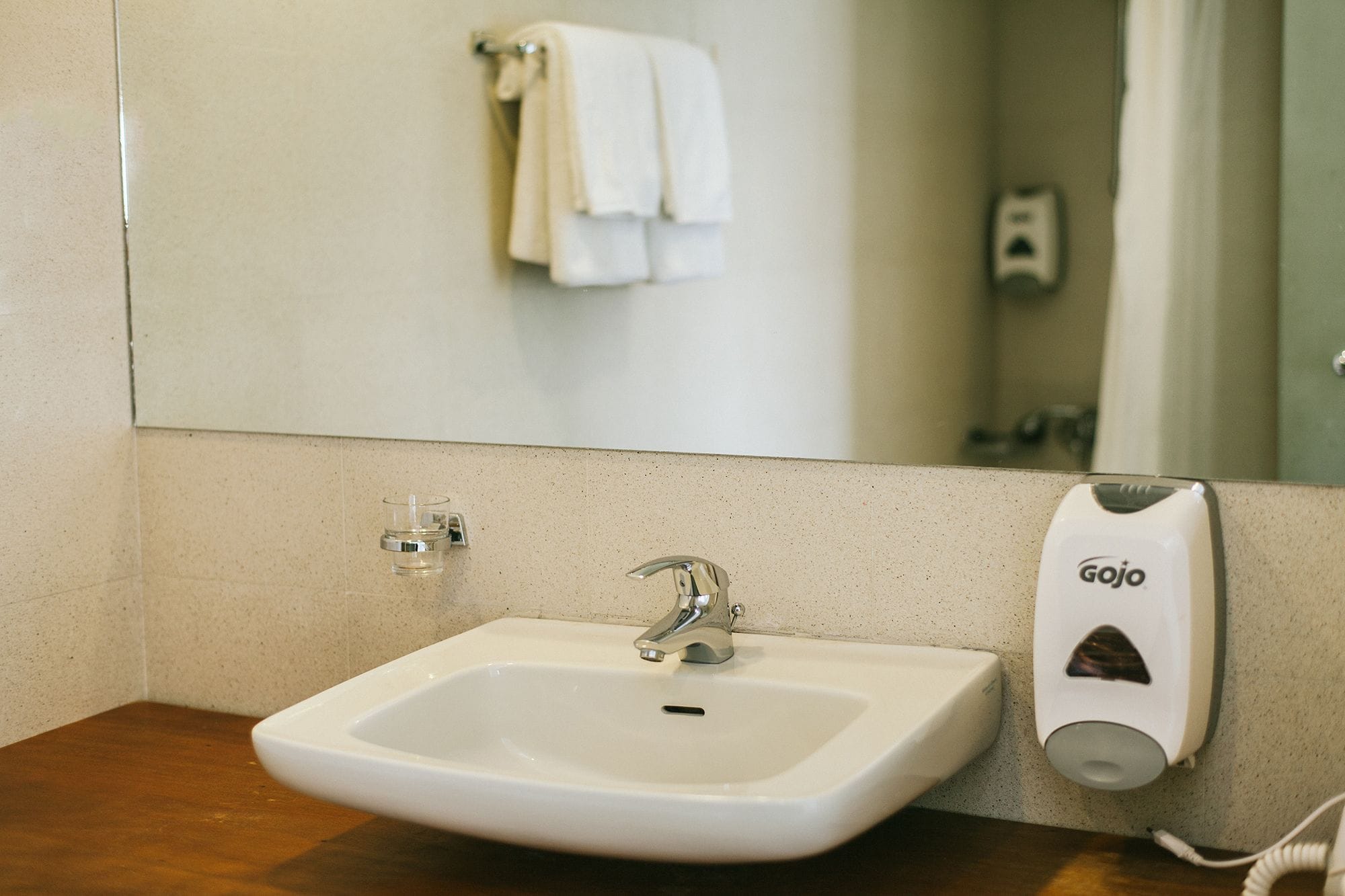 A bathroom with a white sink, a mirror, and a towel hanging on the wall.