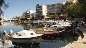 Una marina con barcos amarrados, un hotel llamado "Hotel Du Lac" al fondo y un paseo marítimo con árboles y edificios.
