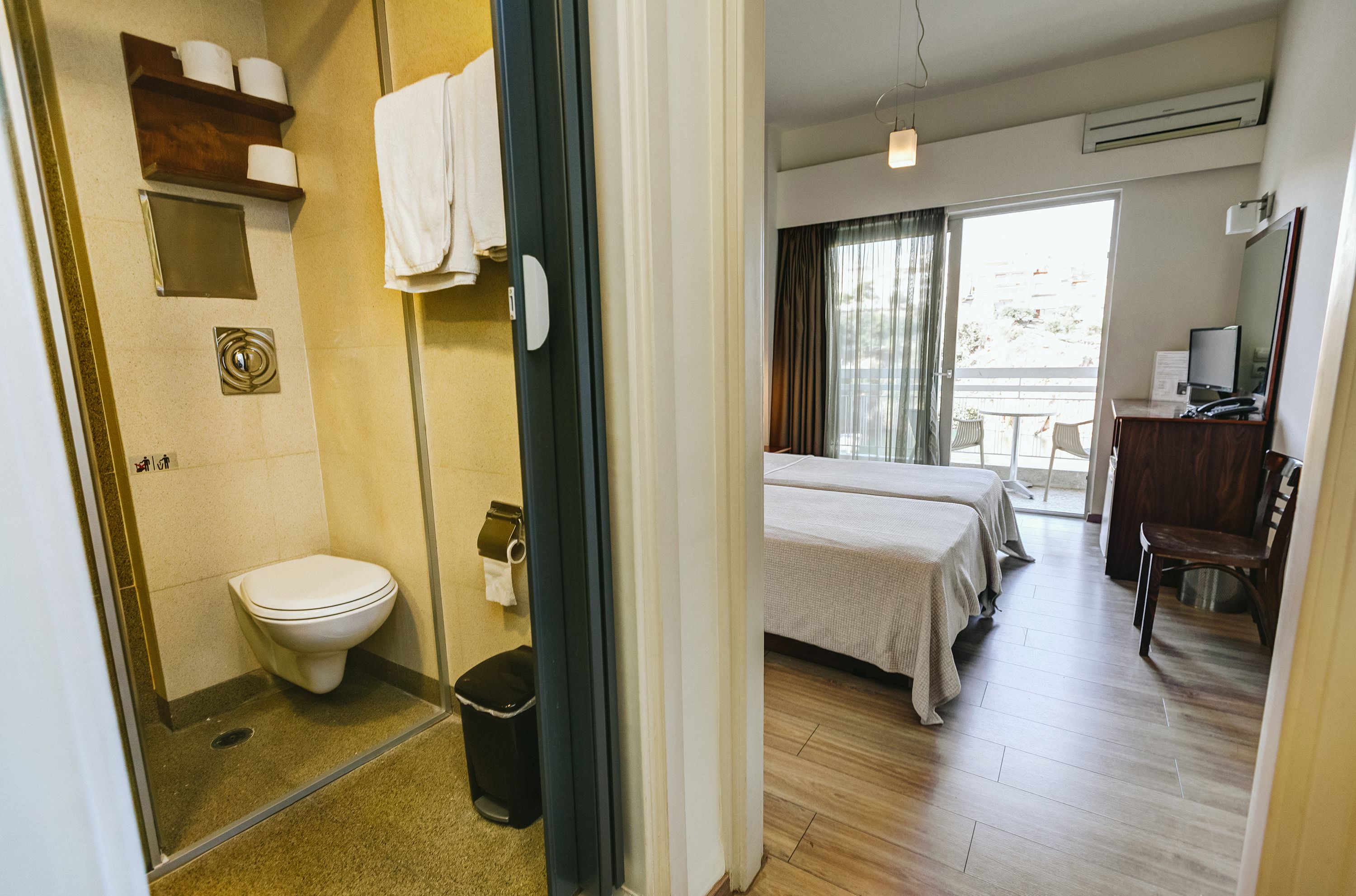 A hotel room with a toilet, shower, and a bed with a view of the outdoors.