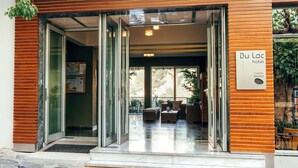 La entrada del Hotel Du Lac, con una puerta de vidrio, un cartel y un área de estar al aire libre visible a través del vidrio.
