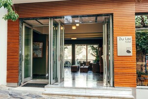 La entrada del Hotel Du Lac, con una puerta de vidrio, un cartel y un área de estar al aire libre visible a través del vidrio.