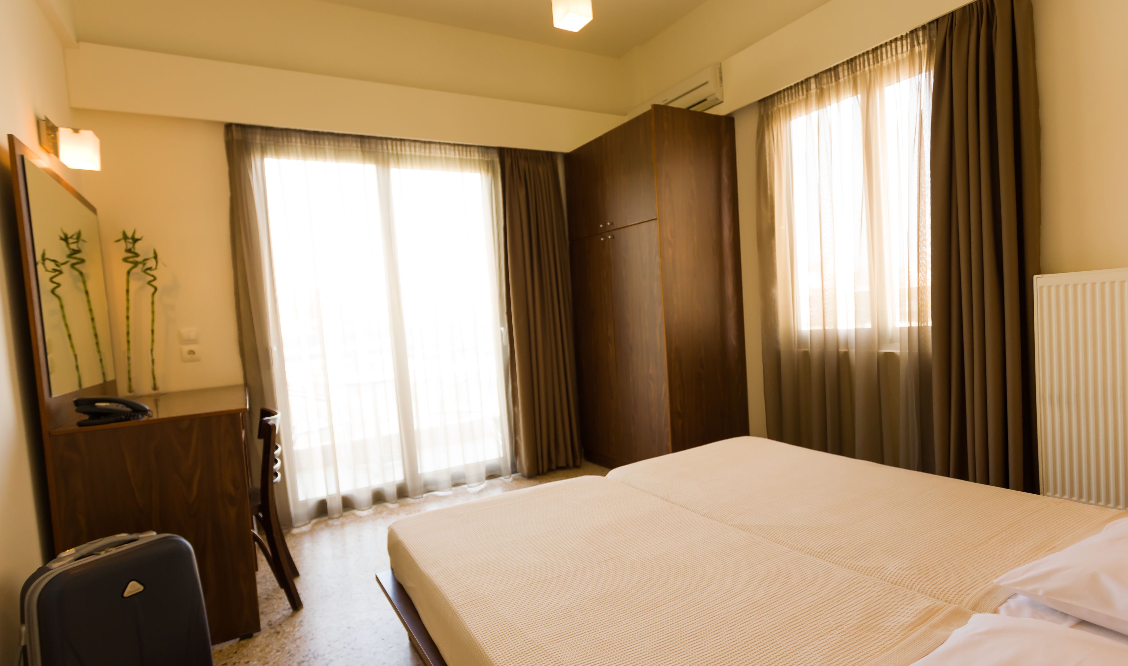 Habitación de hotel con cama, escritorio, silla, espejo y ventana con cortinas.