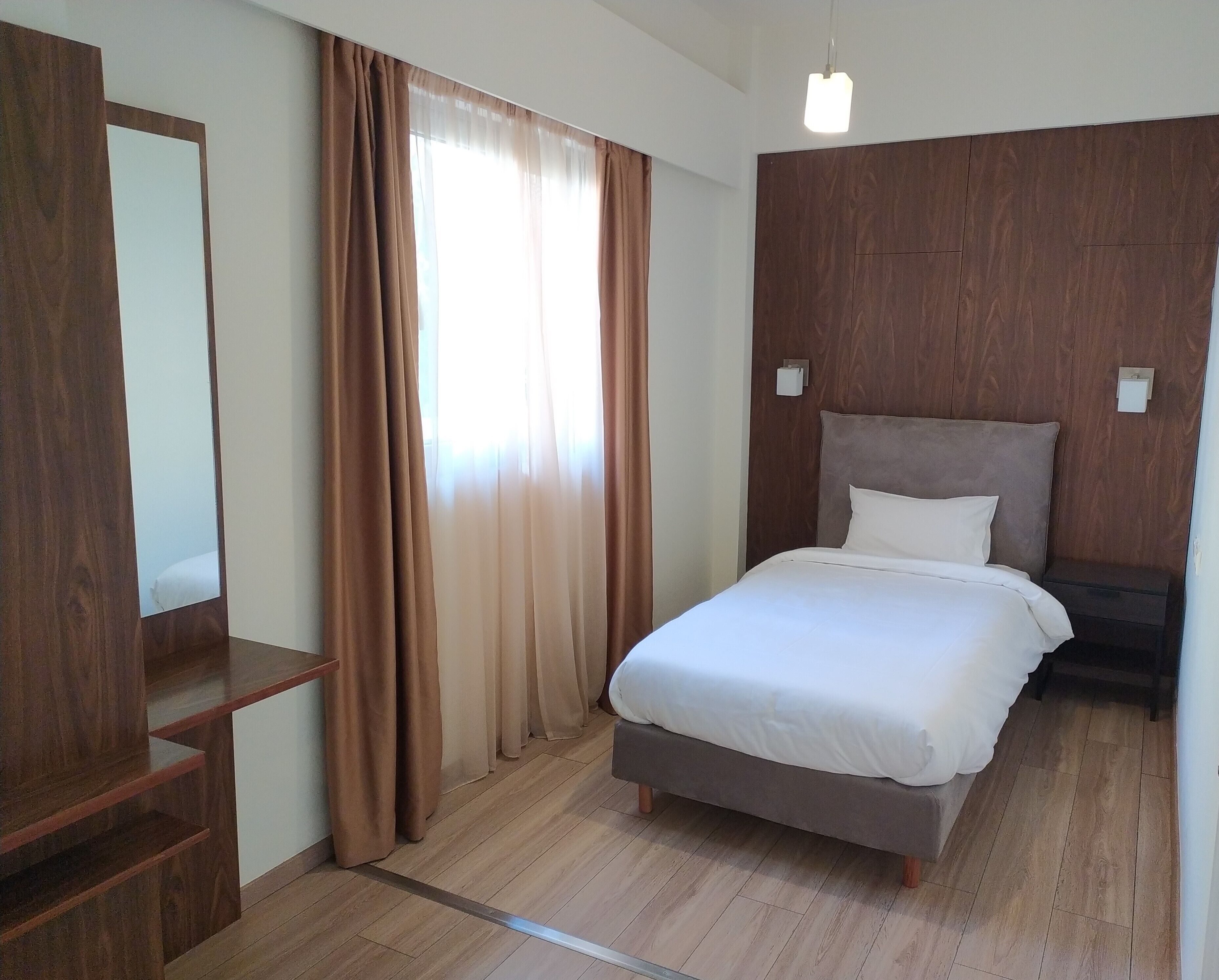 Une chambre d’hôtel avec un lit, une armoire en bois et une fenêtre avec des rideaux.