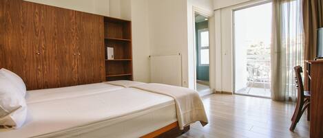 A hotel room with a large bed, wooden headboard, a small bookshelf, a radiator, and a balcony with a view.