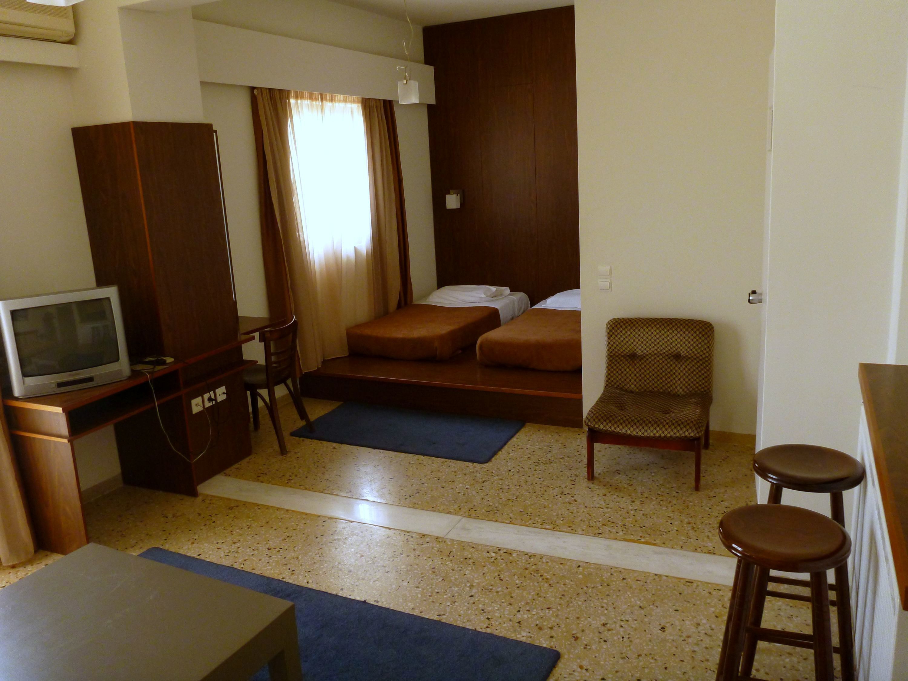 Ein Hotelzimmer mit einem Bett, einem Schreibtisch mit Fernseher, einem Sessel und einem kleinen Hocker.