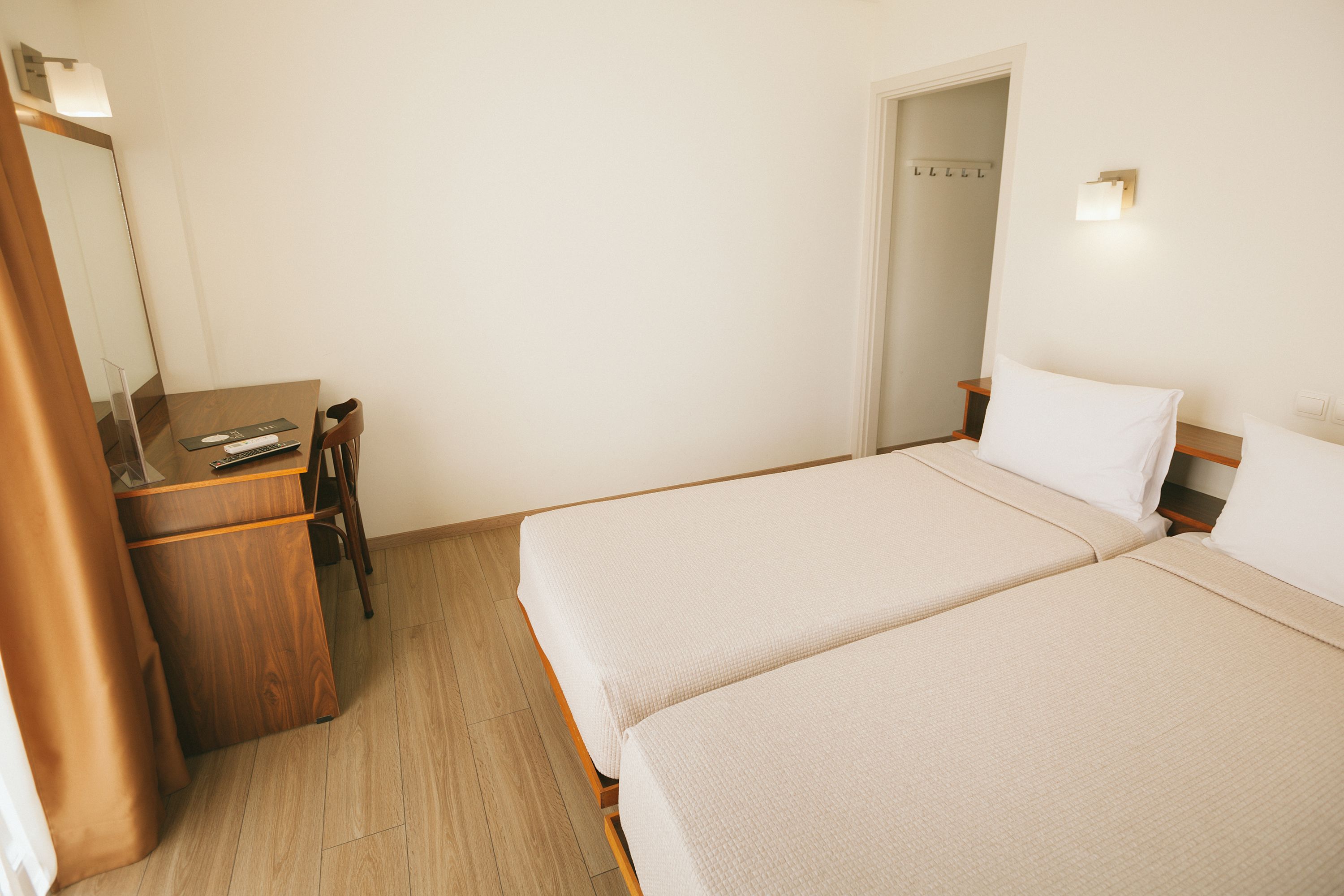 A hotel room with two beds, a desk, a chair, and a mirror.