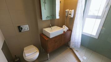 Une salle de bain avec un lavabo blanc, un meuble-lavabo en bois, un miroir, des toilettes et un espace douche.