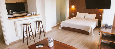 A hotel room with a bed, a TV, a small kitchen area, and a wooden table.