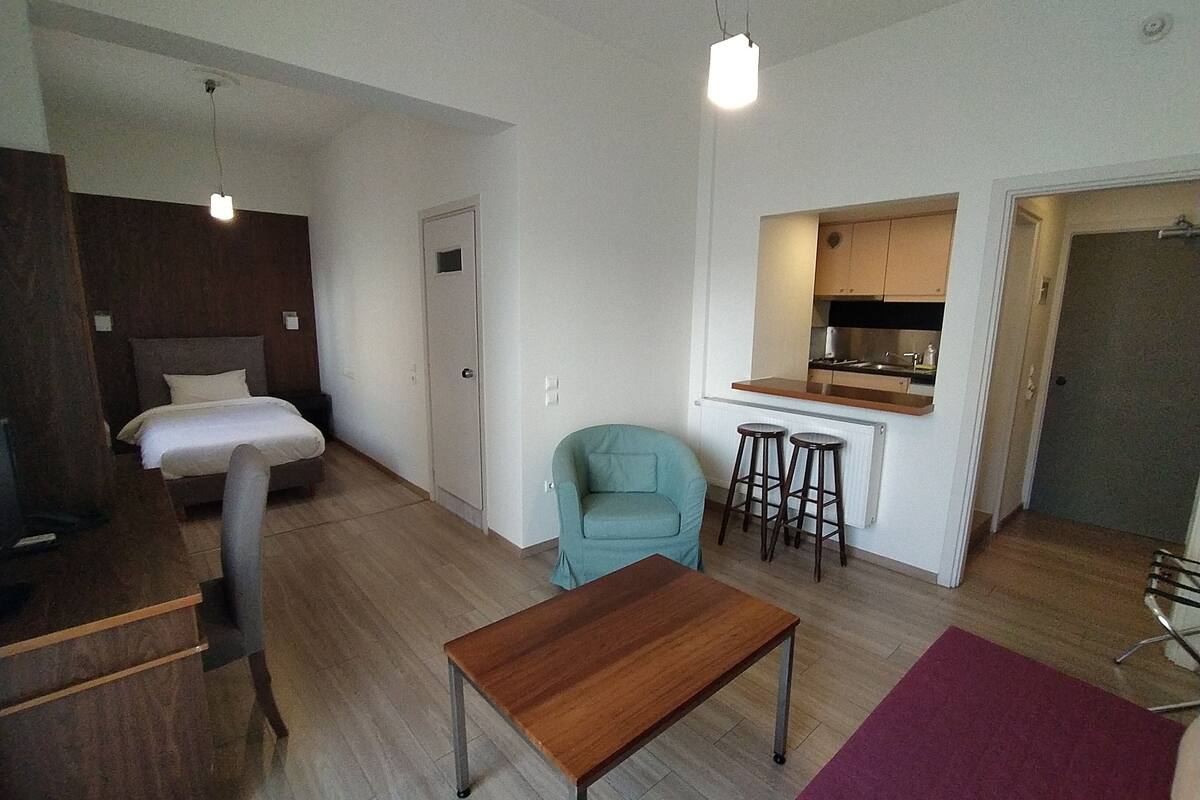 A compact living space with a bed, a small kitchenette, a dining area, and a seating area with stools.