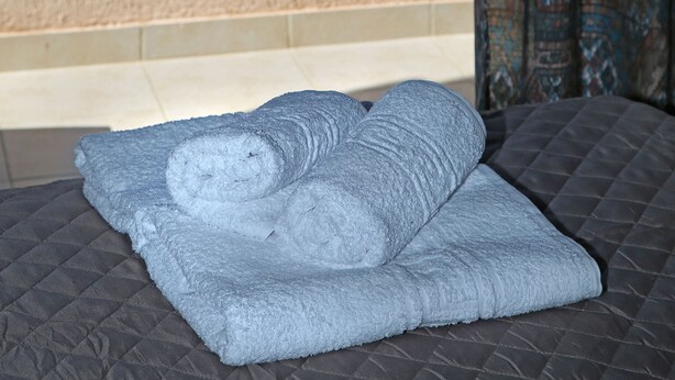 A bed with a rolled-up towel and a view of the ocean through a balcony railing. - Hotel Sea Breeze (Sitia)