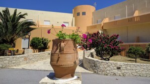 A courtyard with a large terracotta pot, a reception sign, and a building with balconies and a tower. - Hotel Sea Breeze (Sitia)