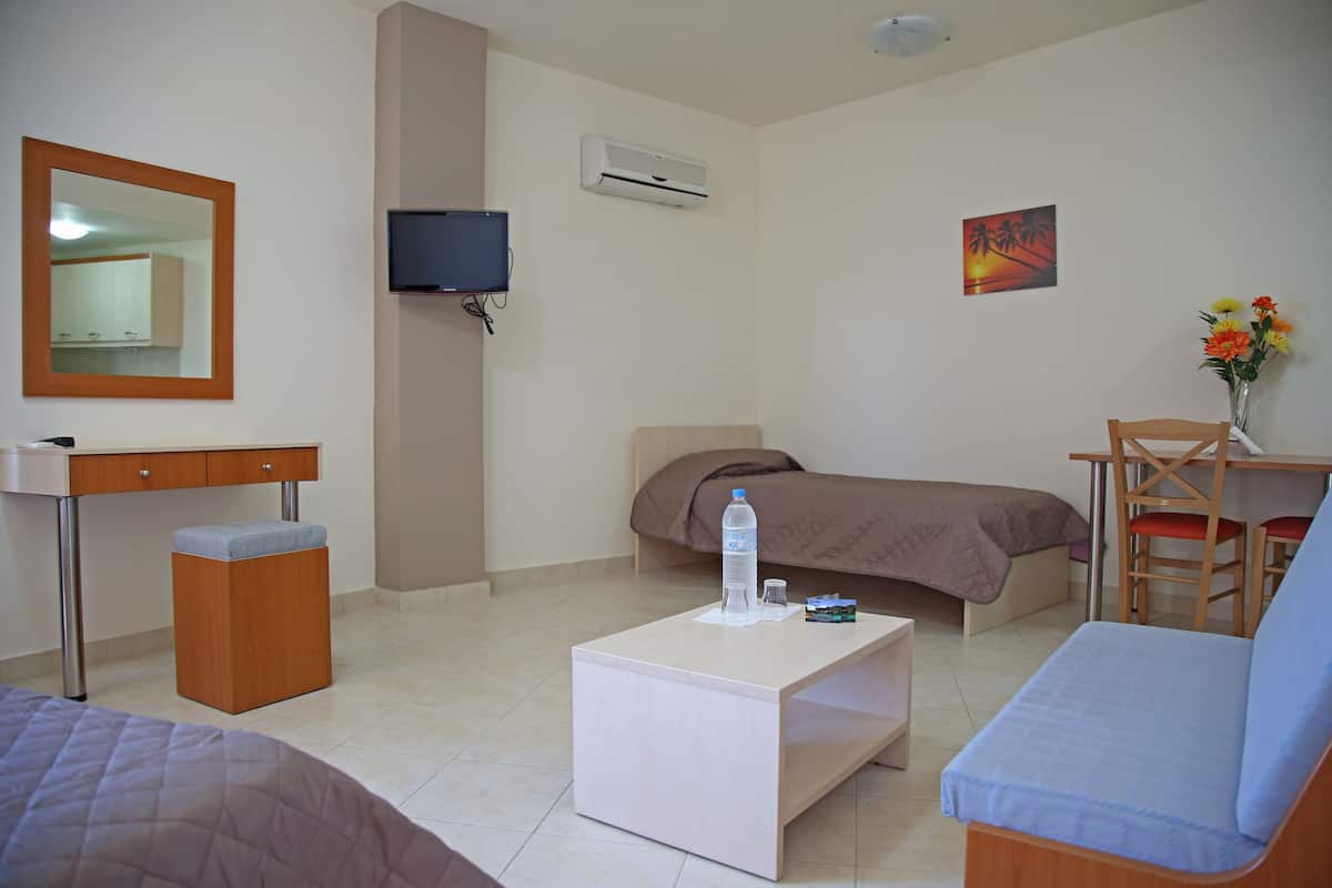 Une chambre d’hôtel comprenant un lit, un bureau, une chaise, une petite table, un miroir, une télévision, un climatiseur et un tableau accroché au mur.