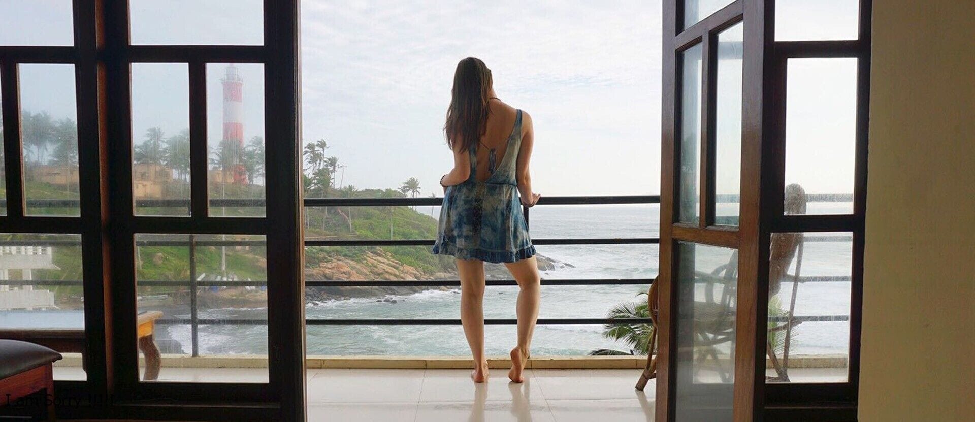 Una mujer de pie junto a un ventanal con vistas a la costa.