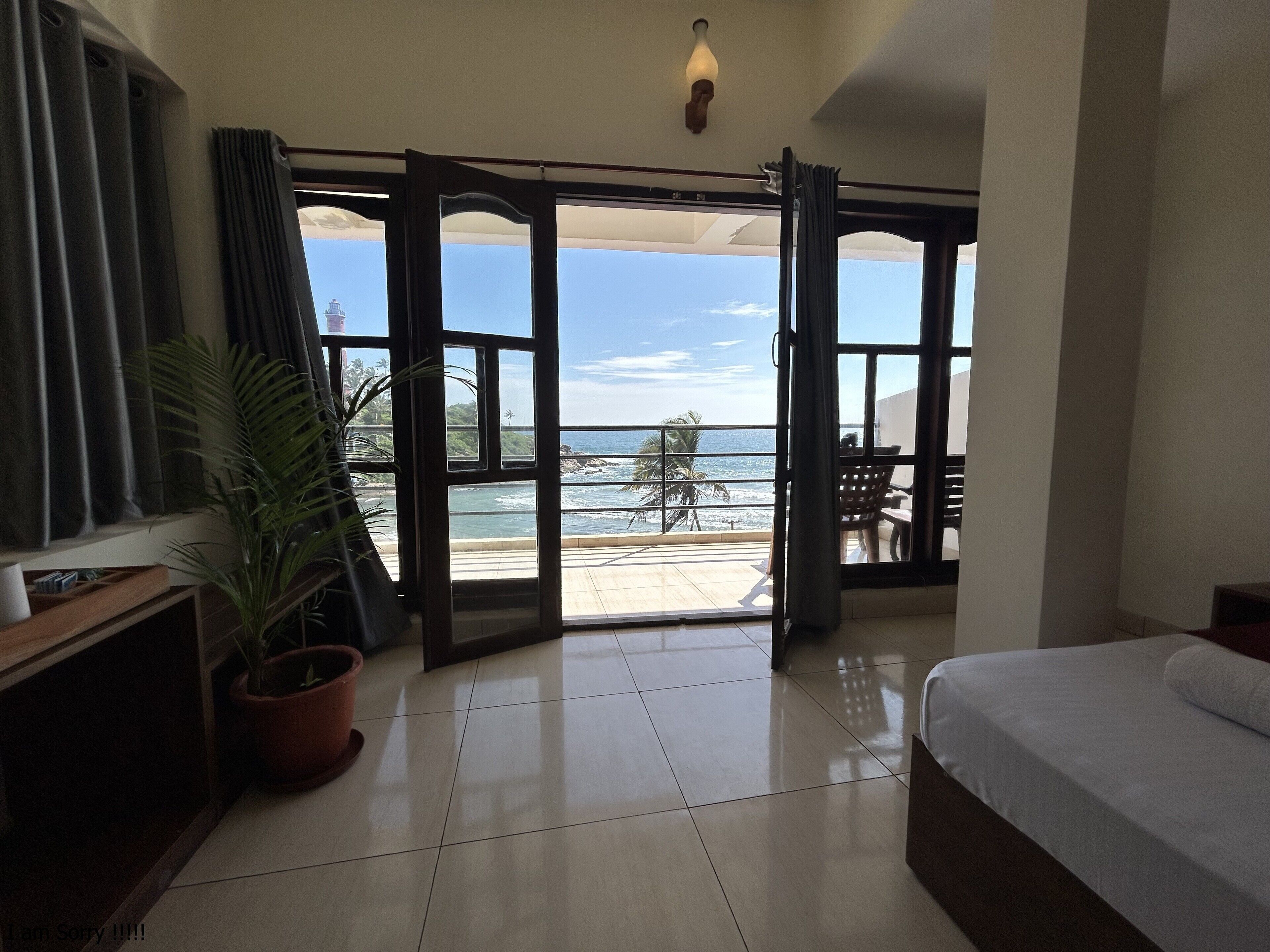 Habitación de hotel con cama, una planta en maceta y vistas a la playa a través de puertas francesas abiertas.