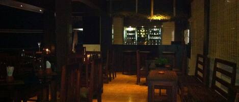 A dimly lit restaurant with wooden furniture and a bar area in the background.