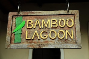 A rustic wooden sign with the text "Bamboo Lagoon" in gold letters, mounted on a wall. - Bamboo Lagoon Backwater Front Resort (Ambalapuzha)