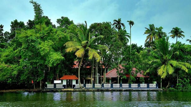 Un hotel a orillas del río con valla blanca, palmeras y edificios de techo rojo.