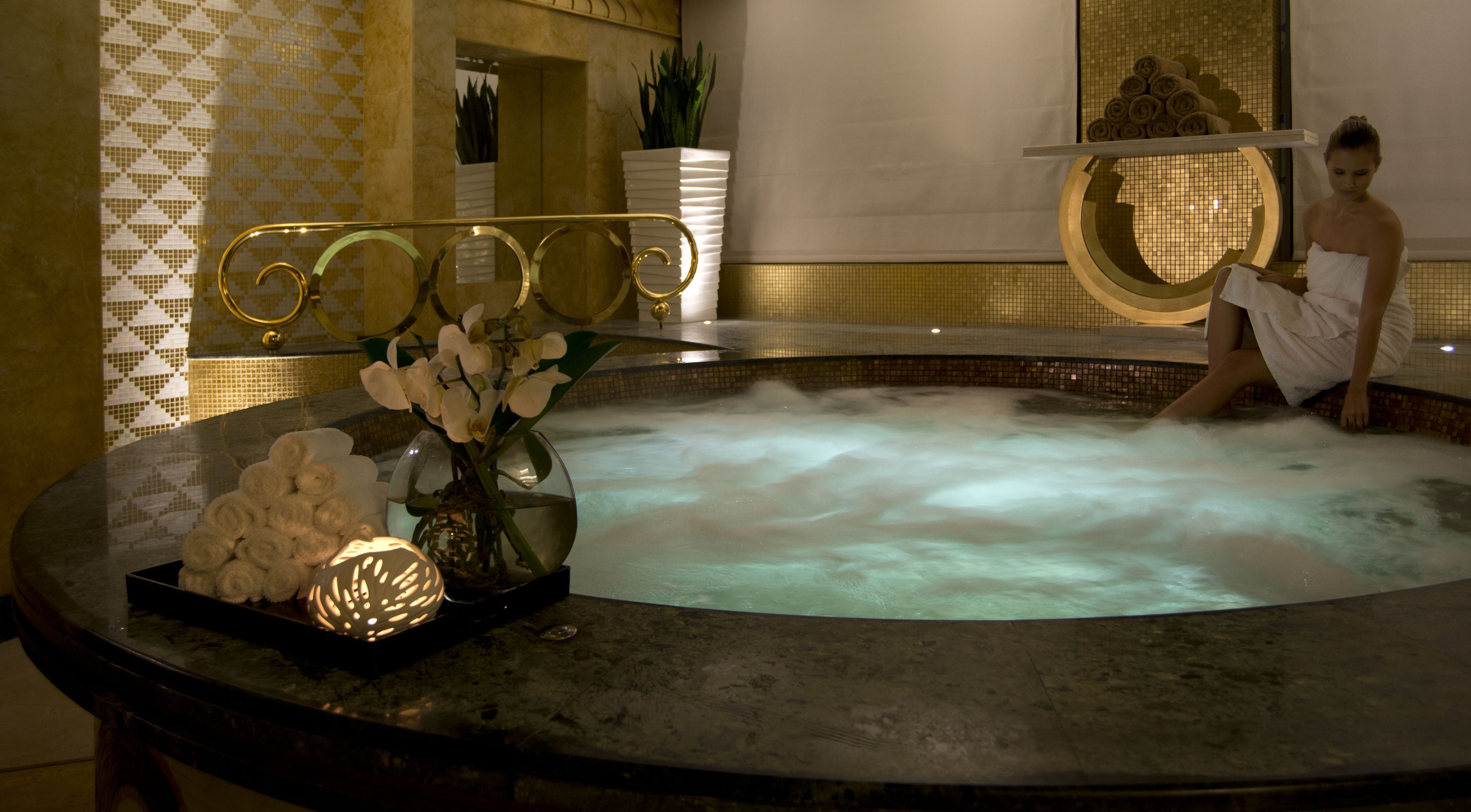 Un bain à remous doté d’un bord en marbre, un vase décoratif contenant des fleurs blanches et un porte-serviettes avec des serviettes.