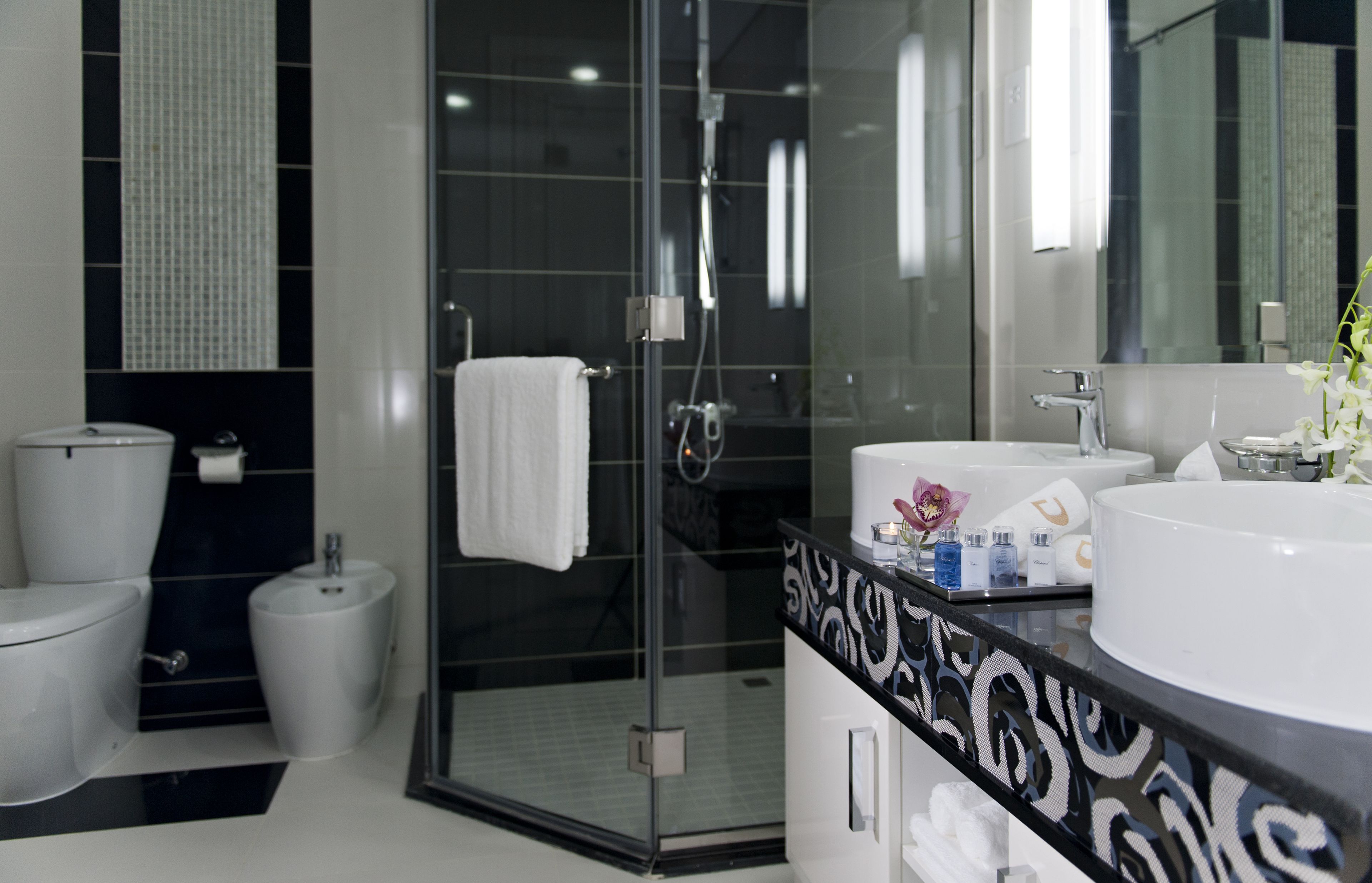 A modern bathroom with a glass-enclosed shower, a white sink, and a black patterned vanity.