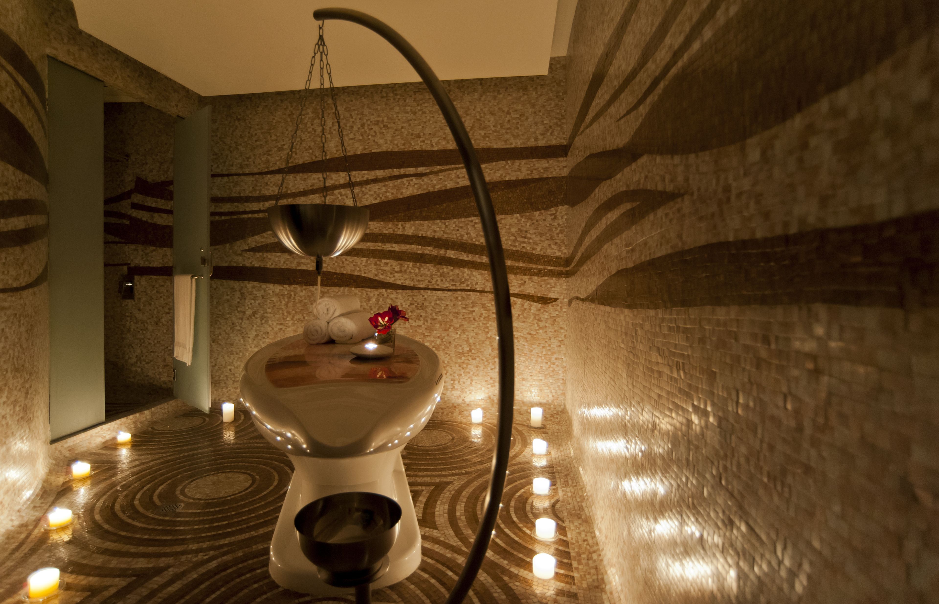 A bathroom with a unique design, featuring a toilet with a bowl-shaped seat, a hanging light fixture, and candles on the floor.