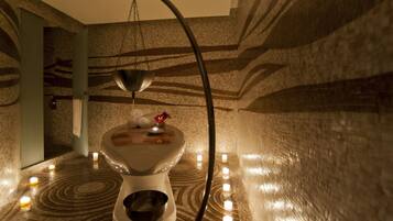A bathroom with a unique design, featuring a toilet with a bowl-shaped seat, a hanging light fixture, and candles on the floor.