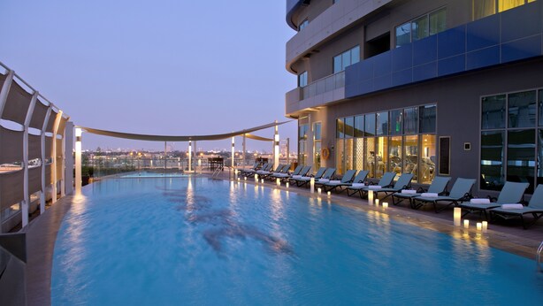 A pool area with lounge chairs and a view of the city skyline at dusk. - DAMAC Maison Mall Street (Dubai)