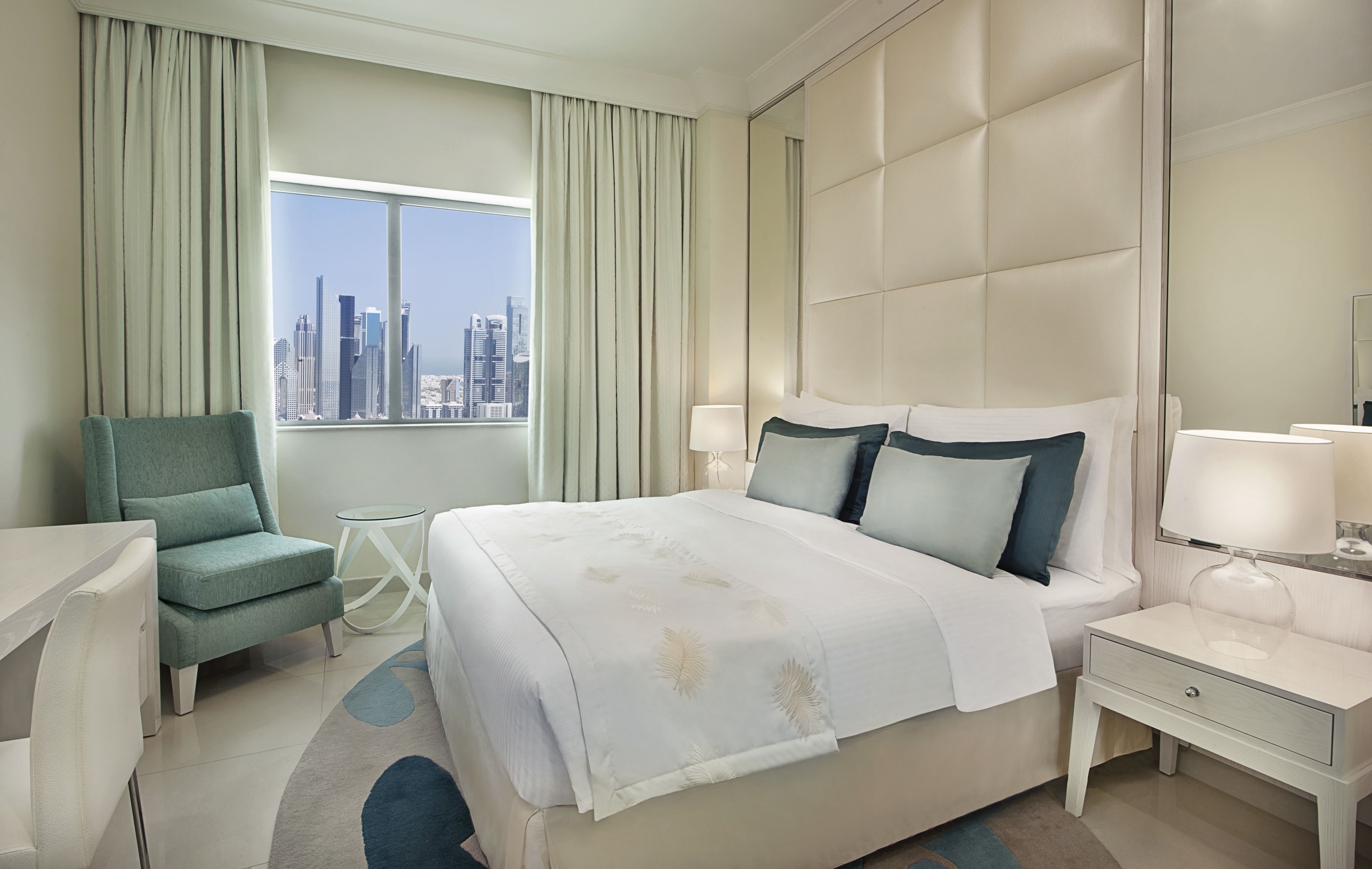 A hotel room with a large bed, a chair, a nightstand, and a view of a city skyline.