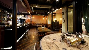 Een bar met houten vloer, een ronde tafel met flessen en een bakstenen muur op de achtergrond.