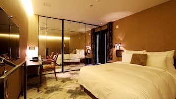 A hotel room with a large bed, a desk, and a chair. There is a mirror on the wall and a window with curtains.
