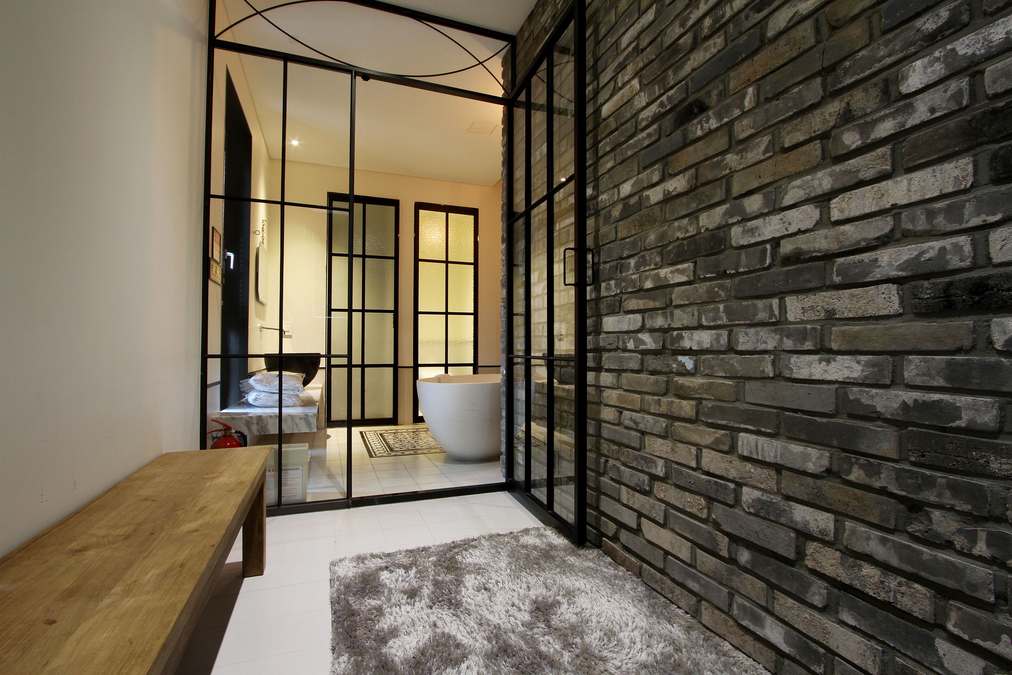 Un baño moderno con una bañera grande, un banco de madera y una pared de ladrillo.