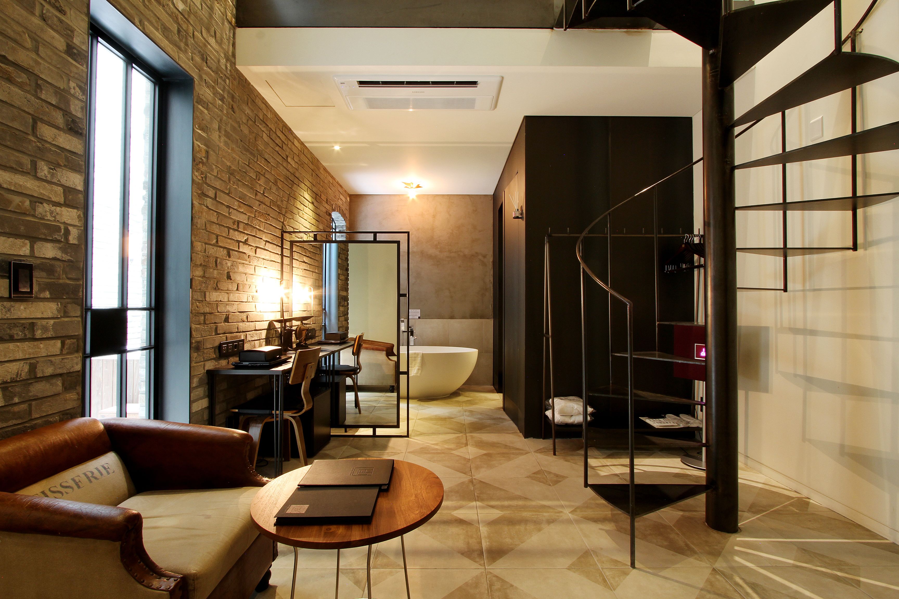 A modern bathroom with a large bathtub, a shower area, and a seating area with a leather couch and table.