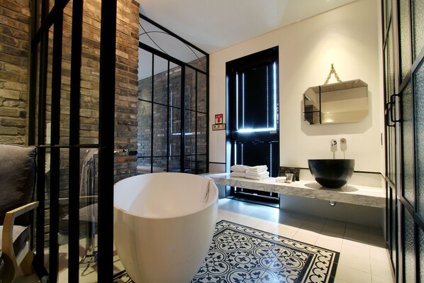 Un baño moderno con una bañera grande, una encimera de mármol y un lavabo de diseño en negro.