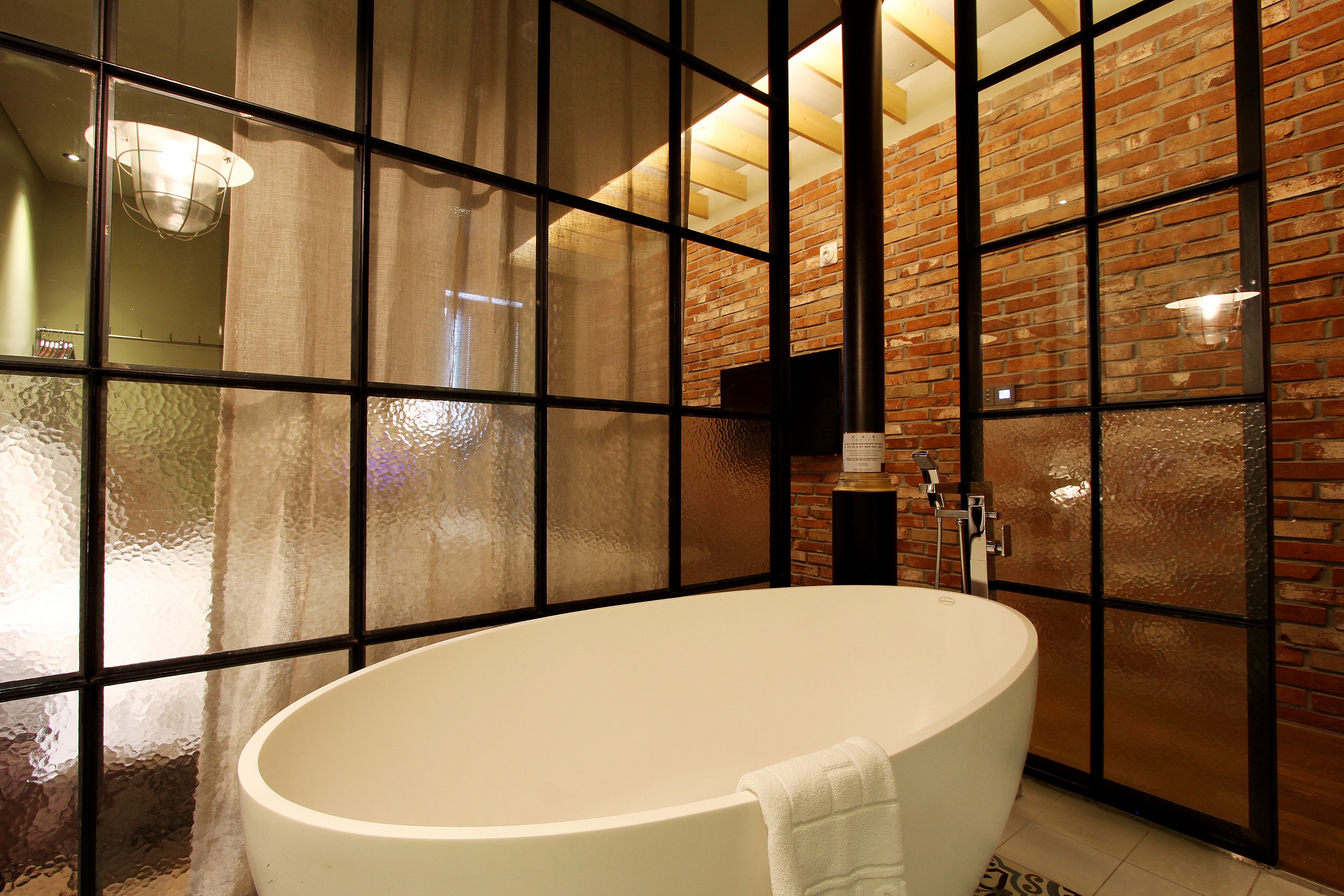 Un baño moderno con una bañera grande, paneles de vidrio esmerilado y una pared de ladrillo.