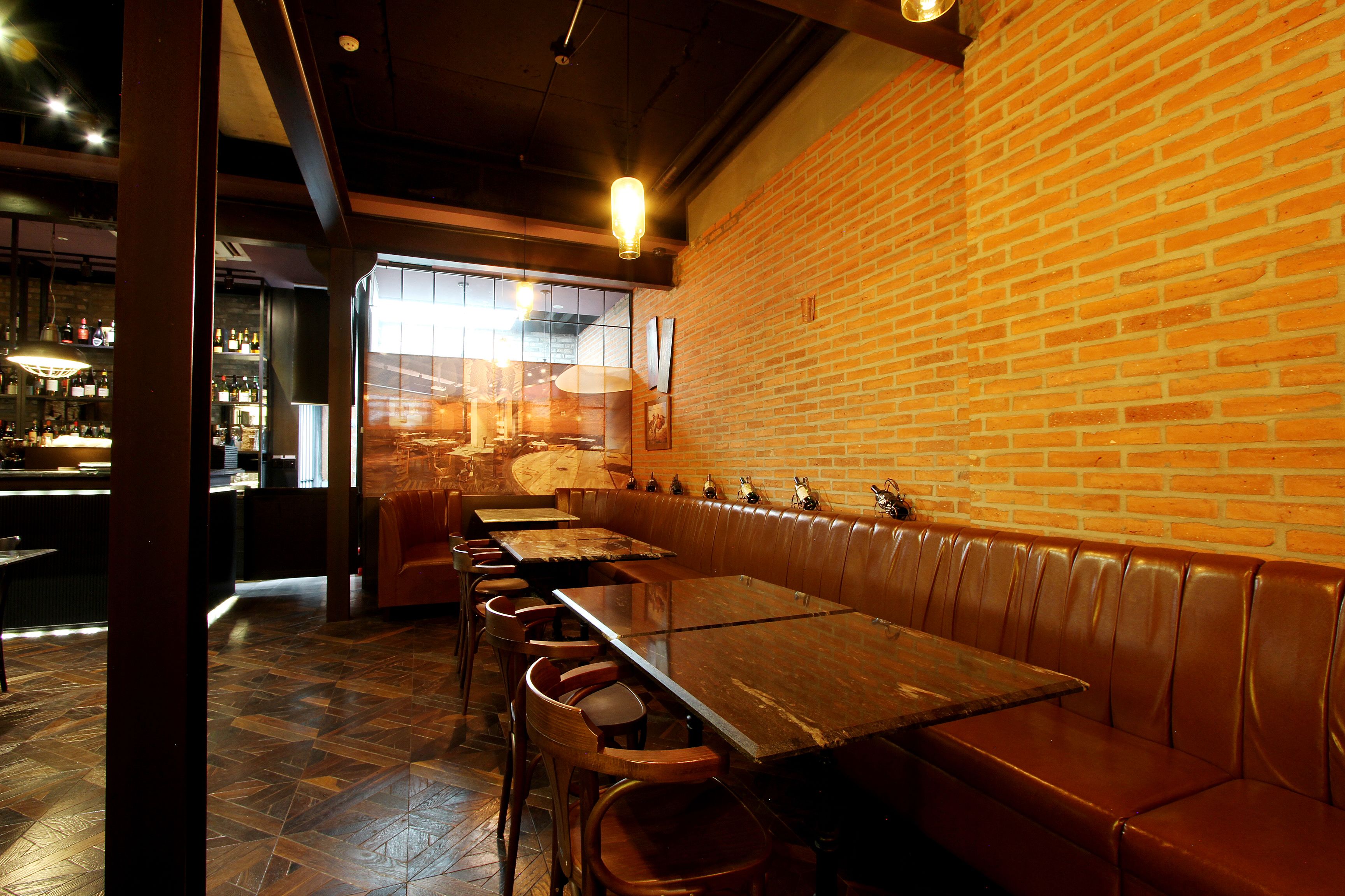 A restaurant interior with brick walls, wooden tables, and leather booths.