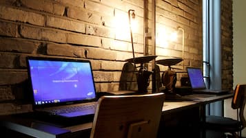 Un espace de travail avec deux ordinateurs portables sur une table, un mur en briques et une fenêtre.