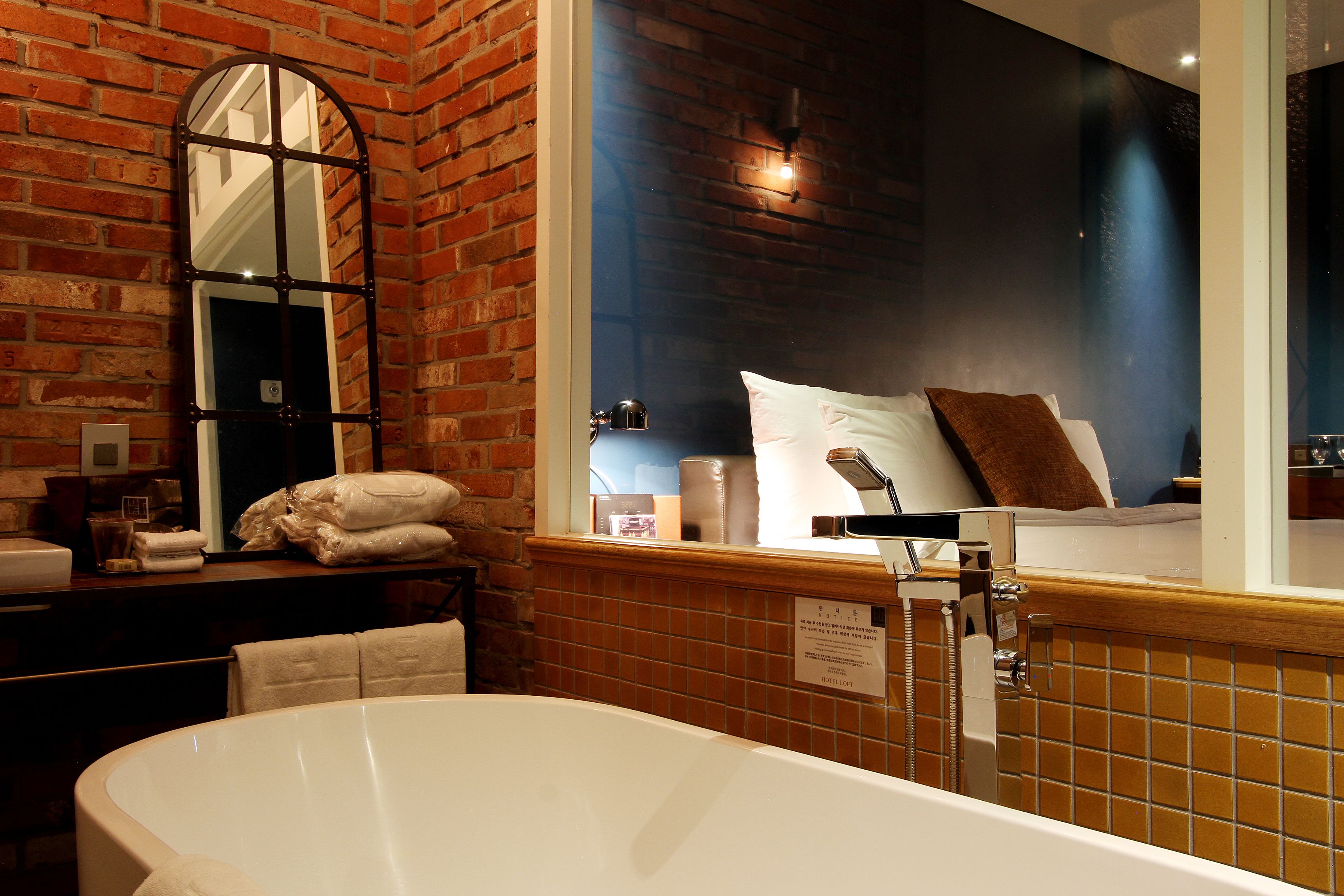A bathroom with a large bathtub, a mirror, and a window with a view of a bed.