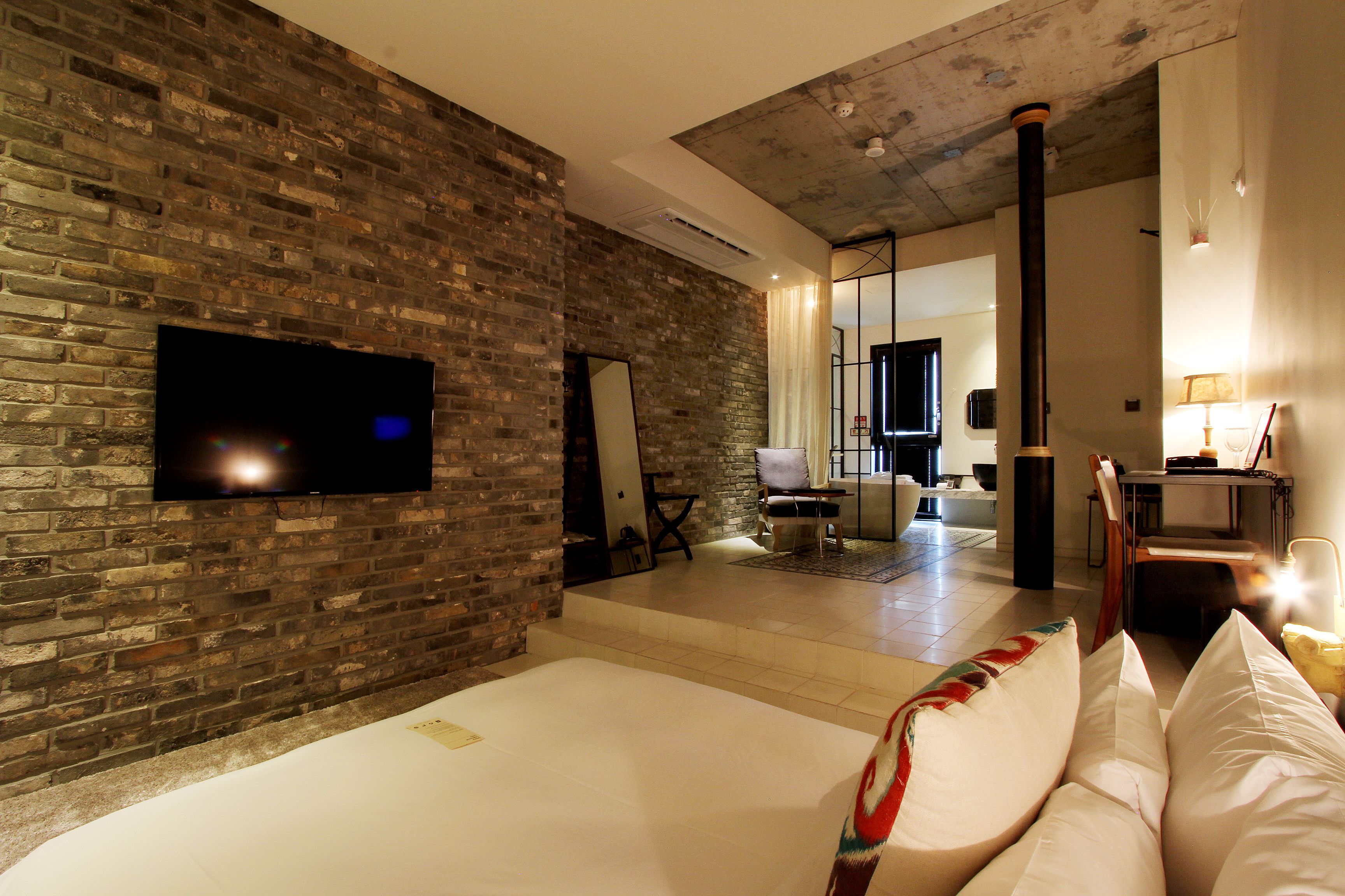 Habitación de hotel con pared de ladrillo, televisor de pantalla plana, cama con ropa blanca y diseño de interiores moderno.