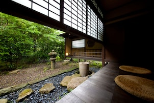A traditional Japanese garden with a wooden walkway, stone lanterns, and a view of a building with large windows.