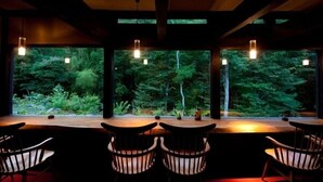 A restaurant with a view of a forest through large windows, wooden tables, and chairs. - Yufuin Gettouan (Yufu)