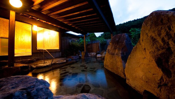 A traditional Japanese onsen with wooden architecture, a stone bath, and a wooden deck. - Yufuin Gettouan (Yufu)