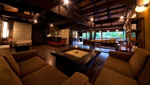 A cozy interior with wooden beams, a central fire pit, and a seating area with sofas and tables. - Yufuin Gettouan (Yufu)