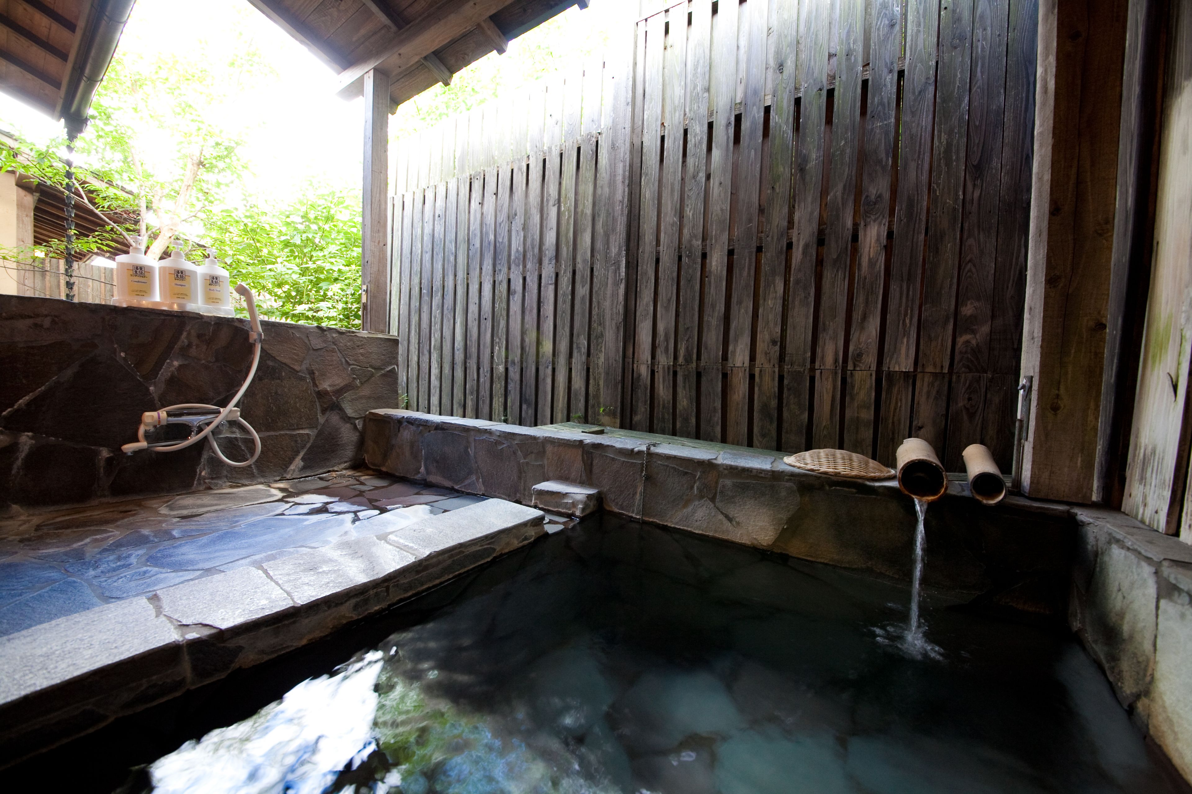 Un bain à remous en pierre, avec une clôture en bois et un mur en pierre.