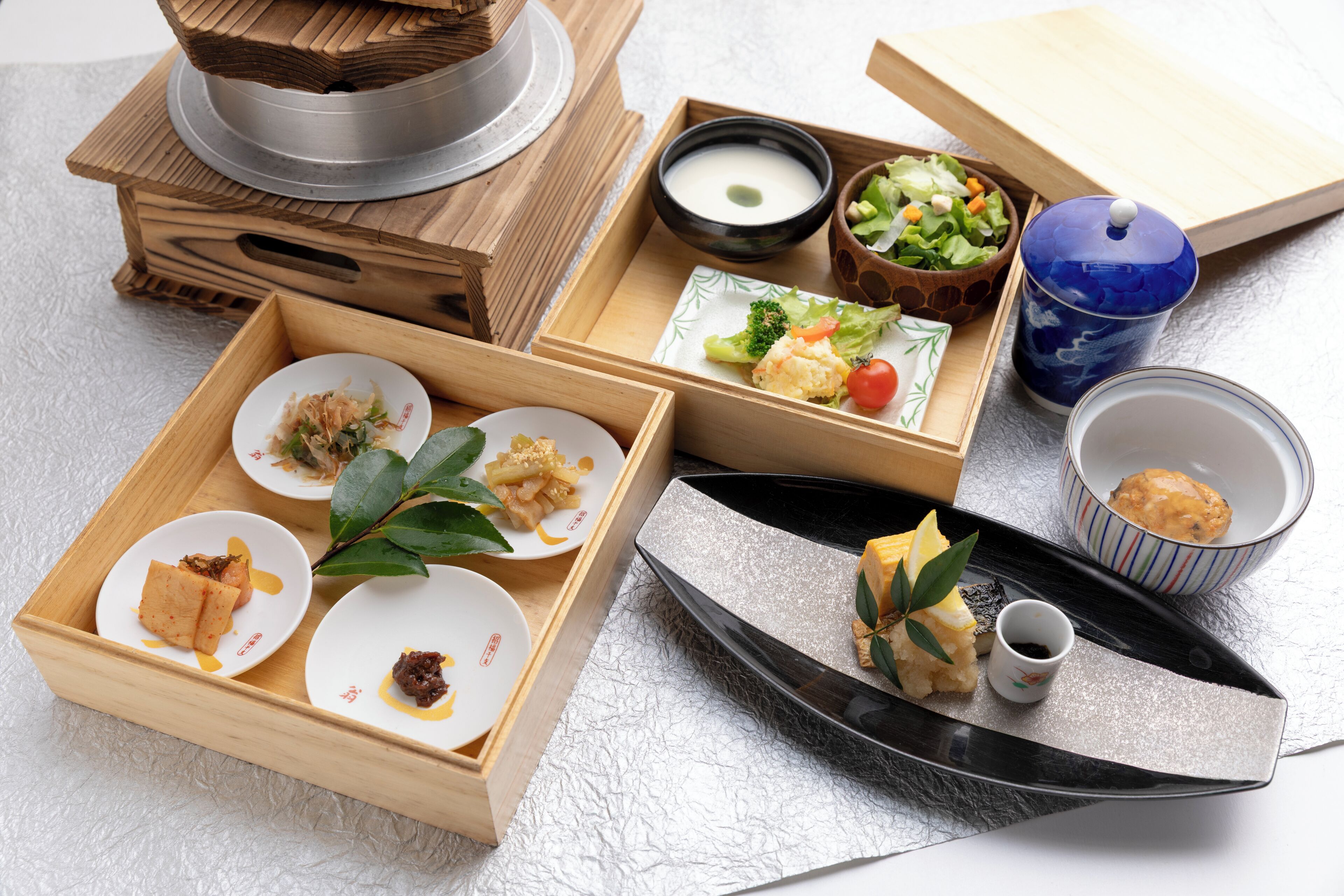 Une variété de plats japonais présentés sur des plateaux en bois et une assiette noire, notamment des sushis, des sashimis et un petit bol de soupe.