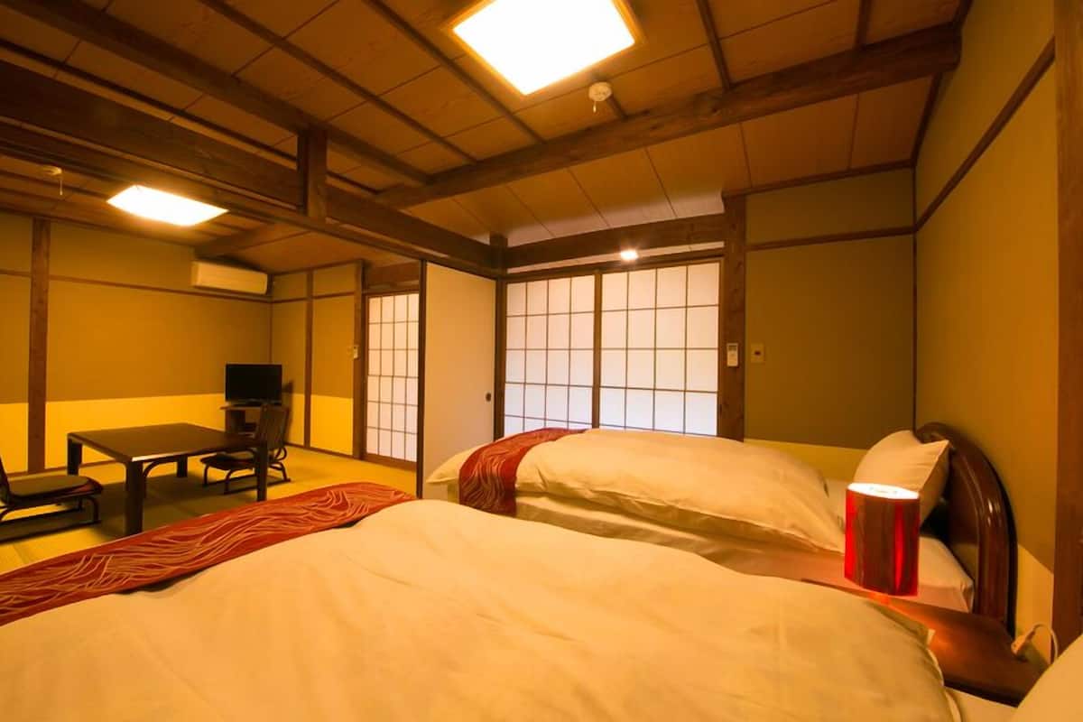 Ein traditioneller japanischer Raum mit Tatami-Boden, einem niedrigen Tisch mit Fernseher und Schiebetüren.