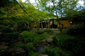 A traditional Japanese garden with a small pond, lush greenery, and a wooden structure. - Yufuin Gettouan (Yufu)