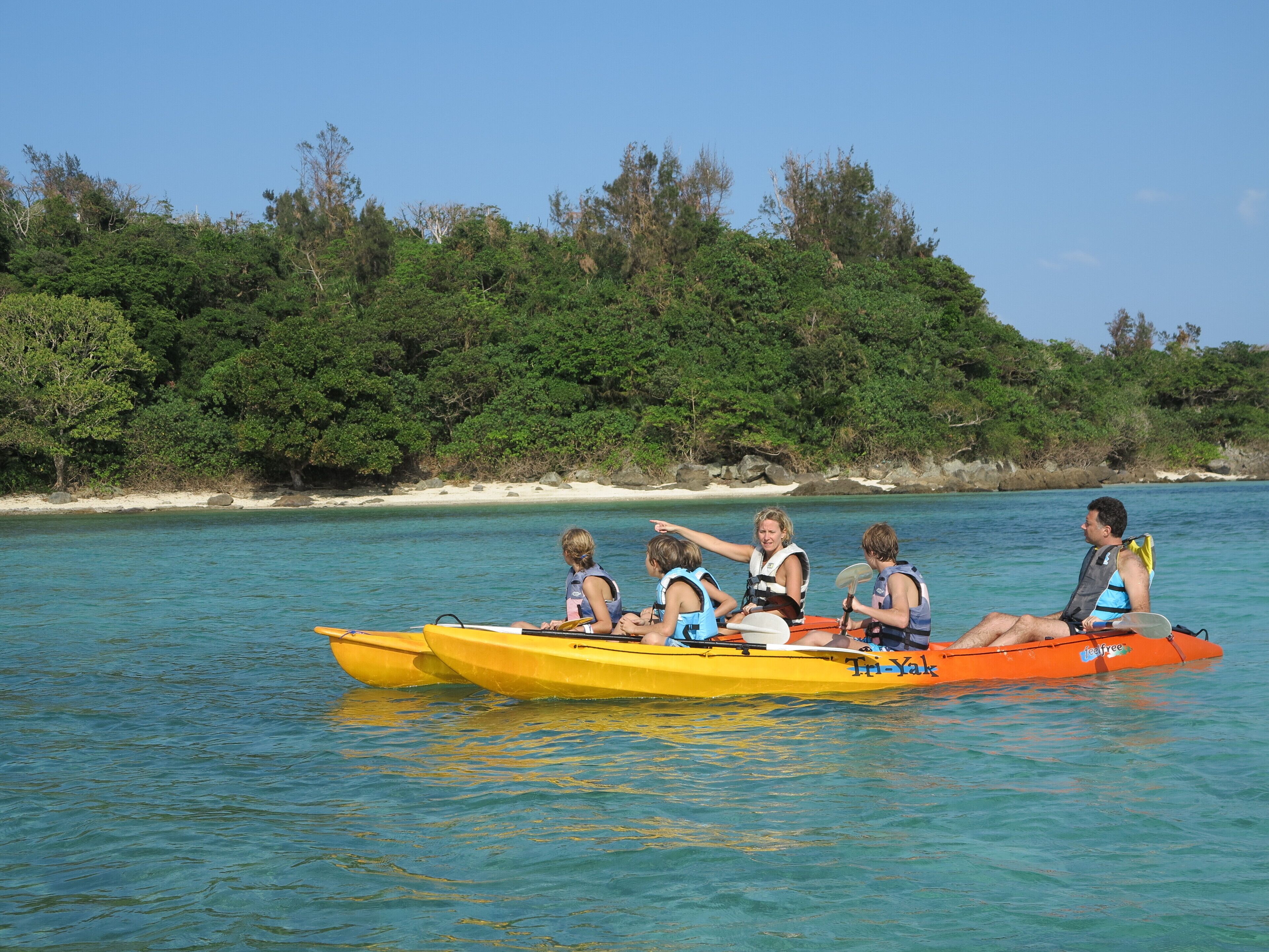 Un grupo de personas en una canoa amarilla y naranja sobre un mar tranquilo, con una isla boscosa al fondo.