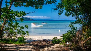 A beach with boats, clear water, and distant mountains.