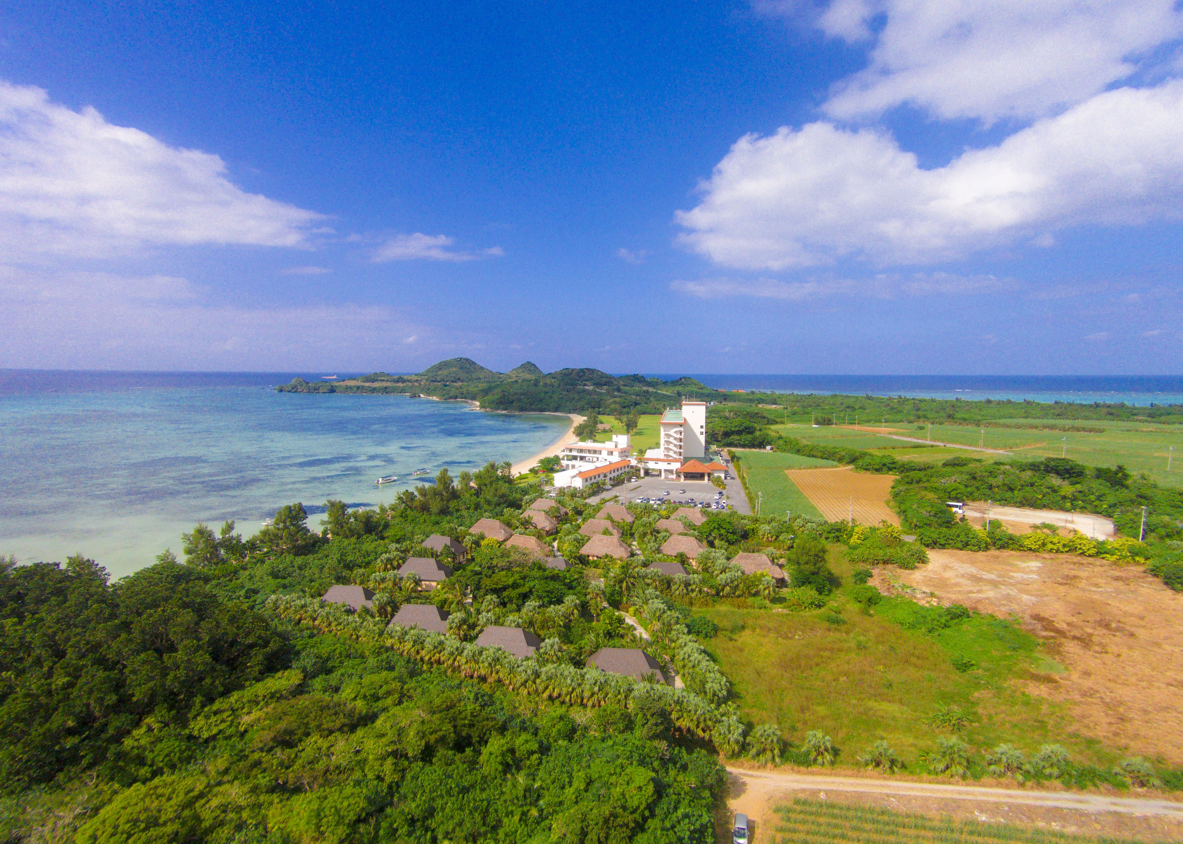 Un resort con varias edificaciones tipo bungaló, una playa y vistas al océano y a islas distantes.