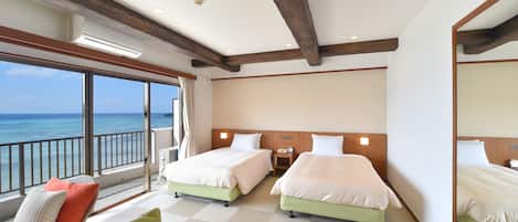 A hotel room with two beds, a balcony with a view of the ocean, and a large mirror.