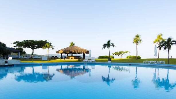 A clear swimming pool with lounge chairs and a thatched-roof pavilion.